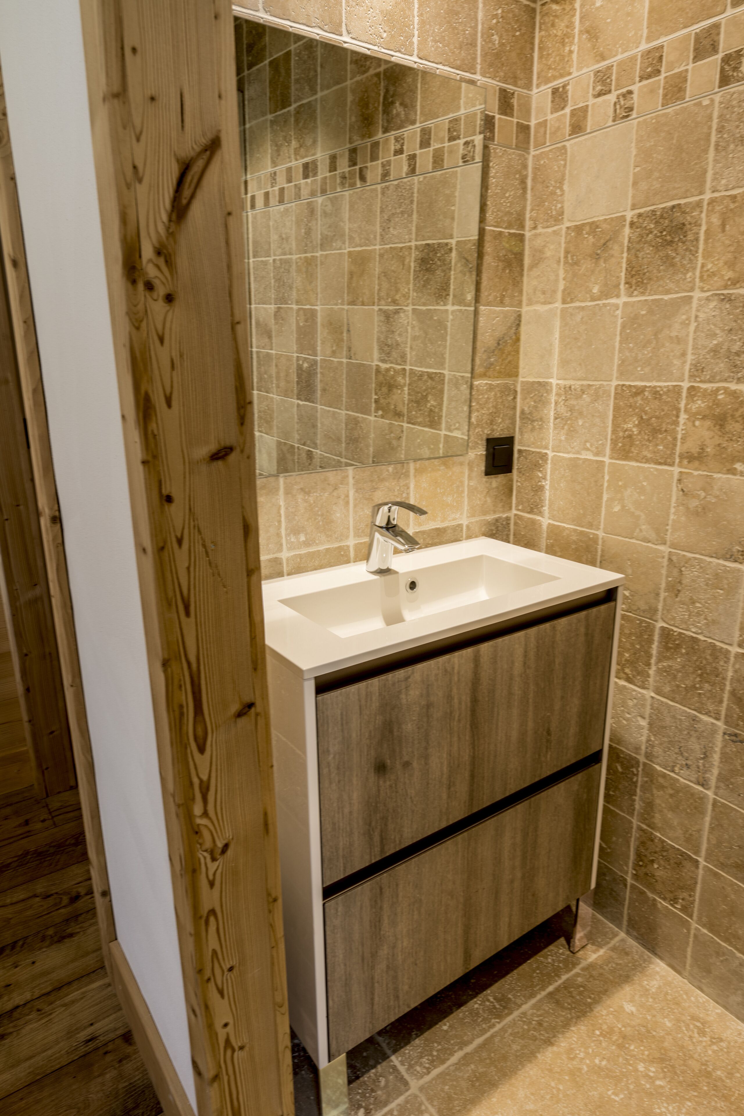 A bathroom with a wooden vanity, a white sink, and a tiled wall.