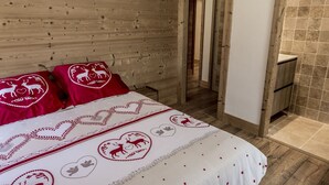 A wooden cabin bedroom with a bed, two red pillows, and a white bedspread with heart patterns. - New apartment in the center of the village and 150 meters from the ski bus. (Samoëns)