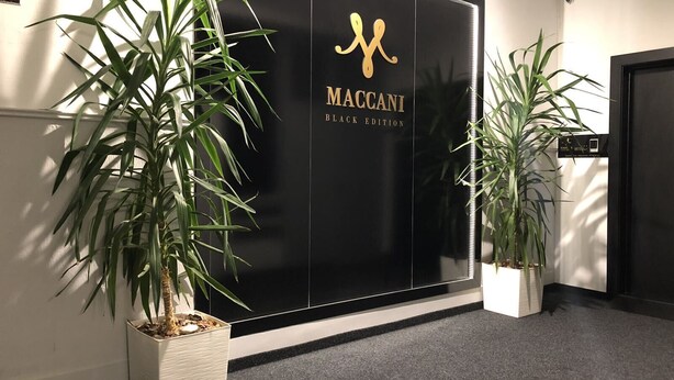 Un mur noir sur lequel est inscrit le texte « Maccani Black Edition », et deux plantes en pot.