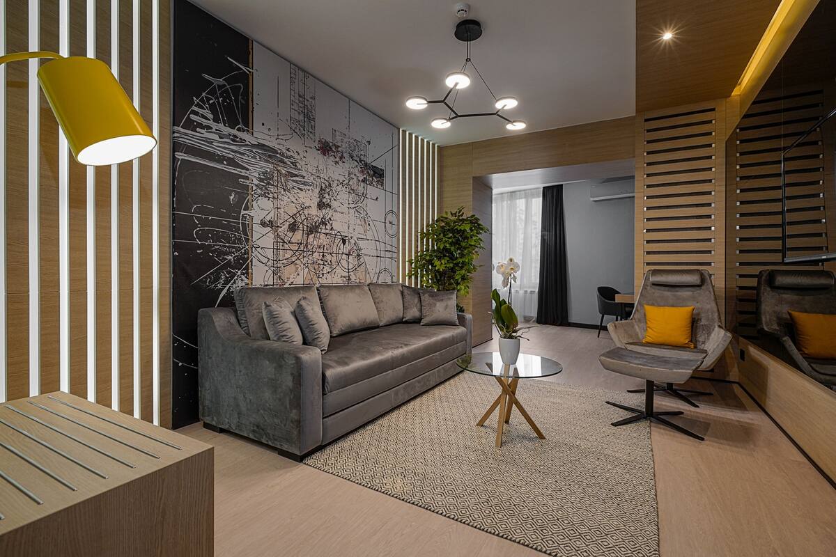 Ein modernes Wohnzimmer mit einem grauen Sofa, einem Glastisch und einer gelben Pendelleuchte.