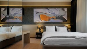 Une chambre d’hôtel moderne avec un grand lit, une table de chevet avec une lampe et deux grandes peintures abstraites au mur.
