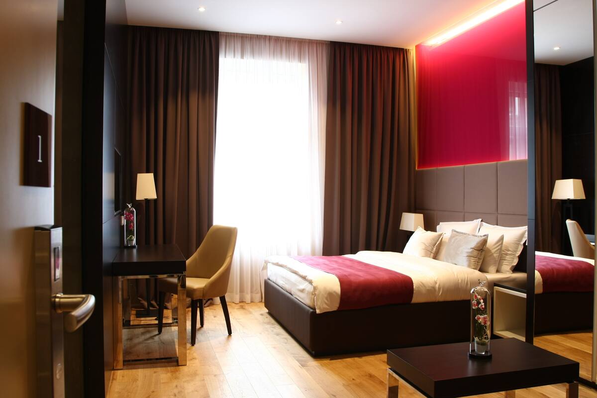 Ein modernes Hotelzimmer mit einem großen Bett, einem Schreibtisch, einem Sessel und einem Nachttisch.