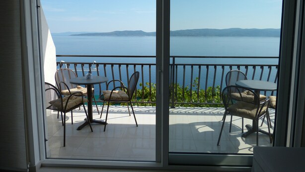 A balcony with a table and chairs, overlooking a body of water and distant land. - Apartment NoStress (Omis)
