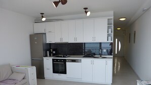 A modern kitchen with white cabinets, a built-in oven, and a dishwasher. There is a small white table with a few items on it. - Apartment NoStress (Omis)