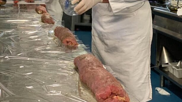 A chef in a white uniform and hat preparing food in a kitchen with stainless steel surfaces and equipment. - Hotel Corona (Cuvio)