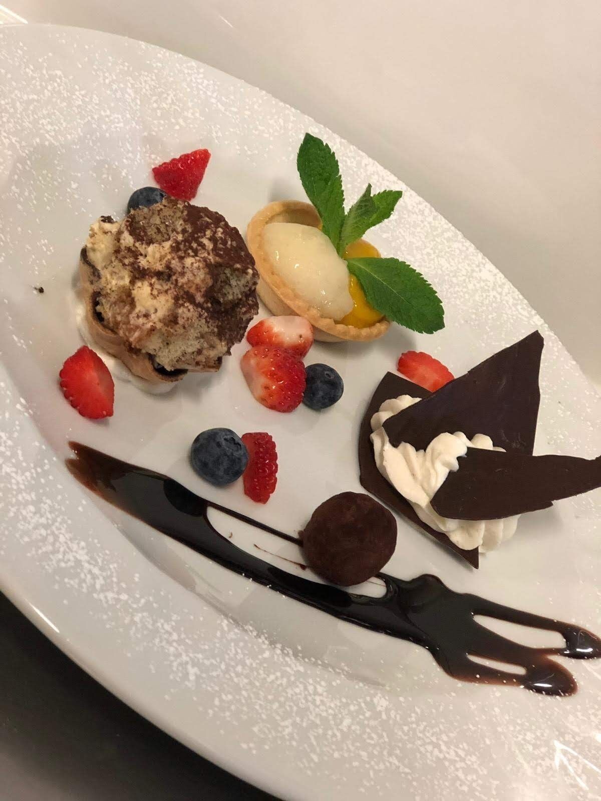 A dessert plate with various items including a slice of cake, a tart, berries, and chocolate.