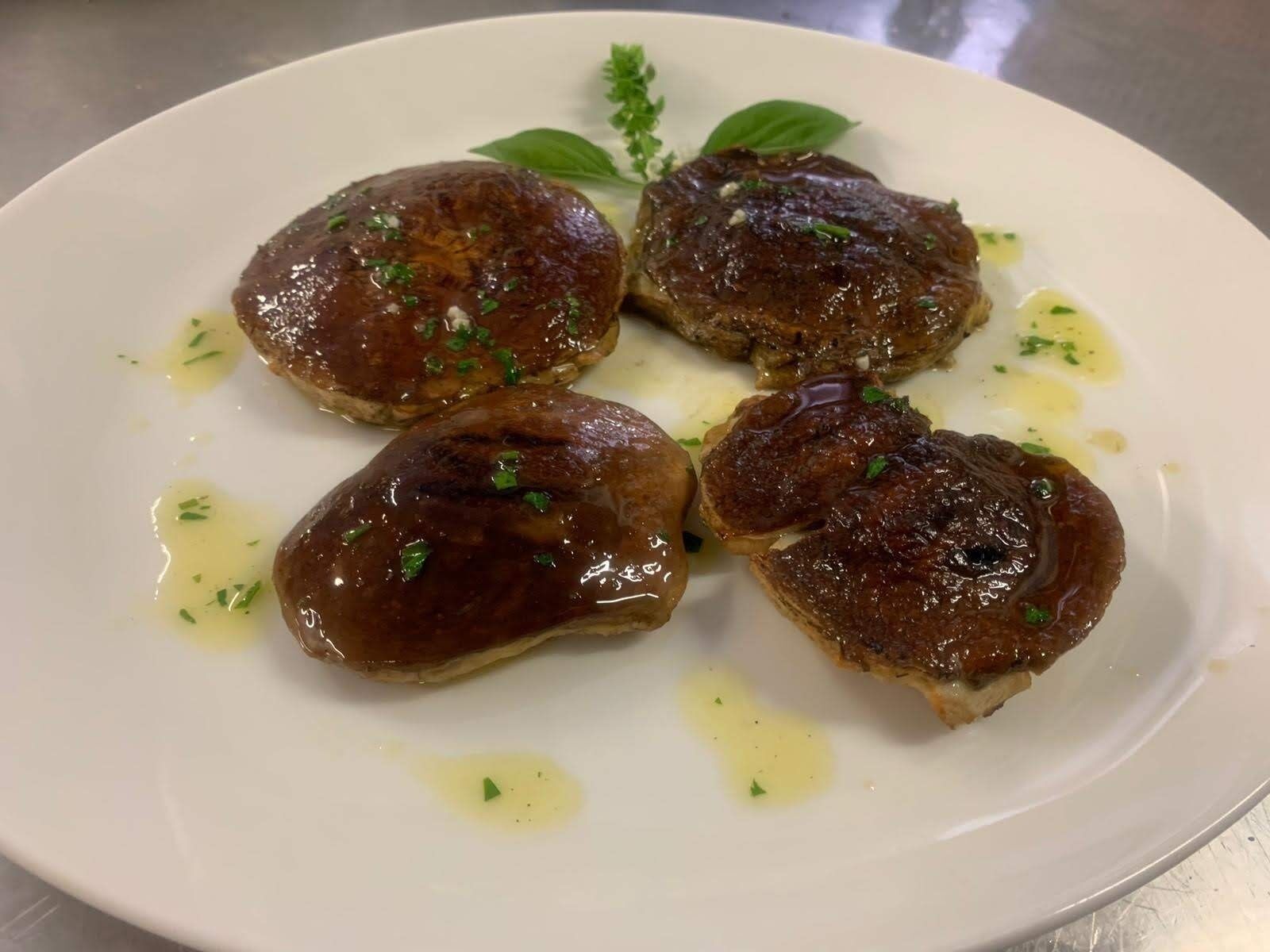 A plate with four glazed meat items garnished with herbs.