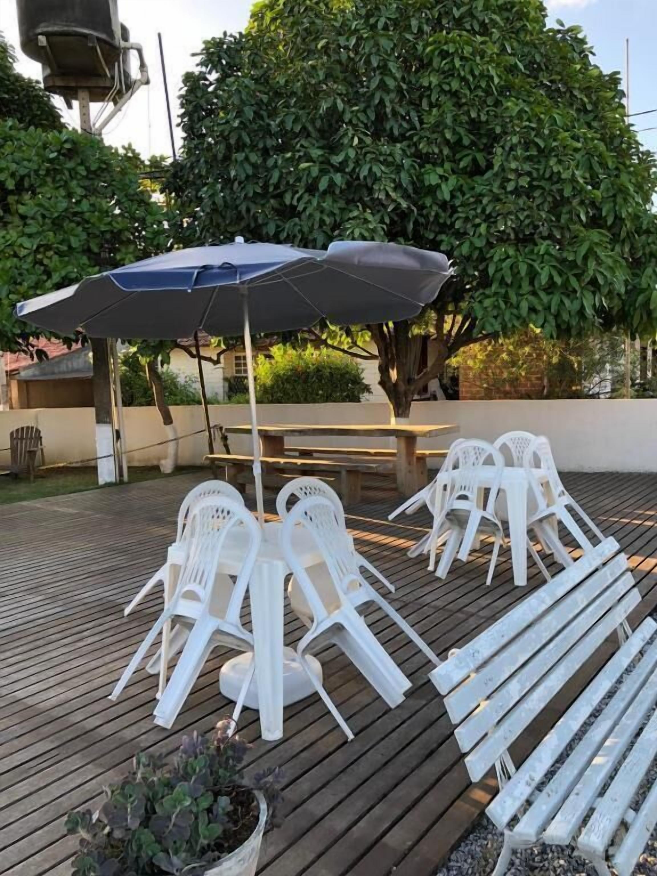 A patio area with white plastic chairs and tables, a large umbrella, and a potted plant.