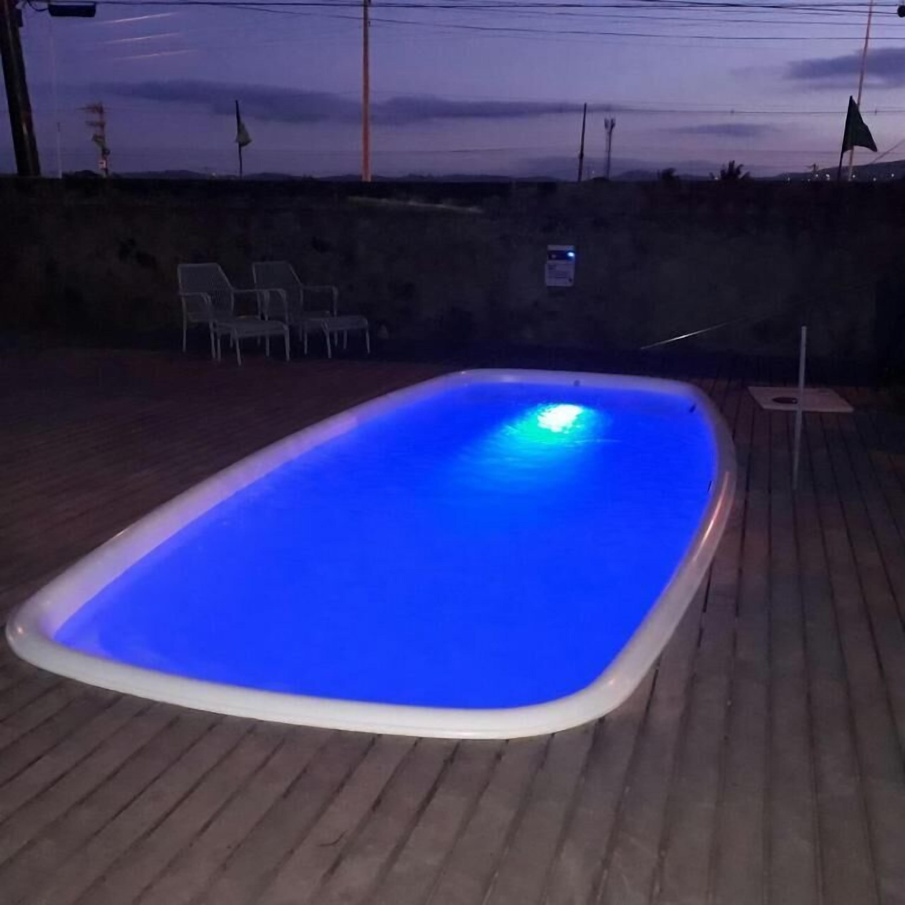 A rectangular swimming pool with a blue light at the bottom, surrounded by a wooden deck.