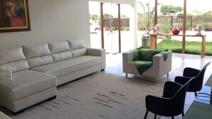 A modern living room with a white sofa, a green armchair, and a coffee table. There is a large window providing a view of the outdoors. - Pousada Vale do Gravatá (Gravata)