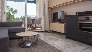 A modern living room with a sofa, a round coffee table, a TV, and a kitchen area with an oven.
