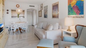 A modern living room with a sofa, armchairs, a coffee table, and a dining area with a table and chairs. - Apartment in Medina Garden for 2 people | 552 (Puerto Banús - Marbella)