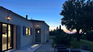 Uma casa moderna com entrada bem iluminada, um caminho de brita e área de estar ao ar livre.