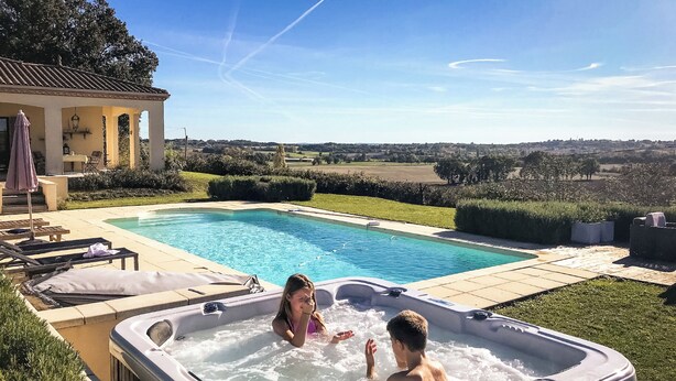 Uma banheira de hidromassagem com duas pessoas, uma piscina e uma área de terraço com espreguiçadeiras.