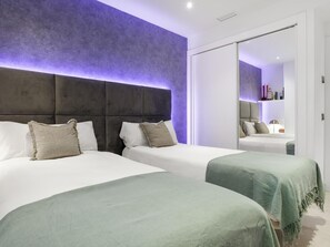 Une chambre d’hôtel avec deux lits, un grand miroir et un mur de couleur violette.