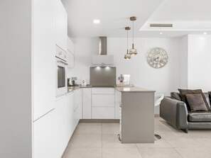 A modern kitchen with white cabinetry, a central island, and a dining area with a grey sofa.