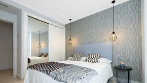 A modern bedroom with a large bed, two bedside tables, a mirror, and a textured wall. - Apartment in Playas del Duque for 4 people| Casa Granada 232 (Puerto Banús - Marbella)
