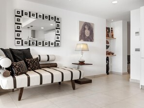 A modern living room with a sofa, a side table with a lamp, a large mirror, and a framed artwork on the wall.
