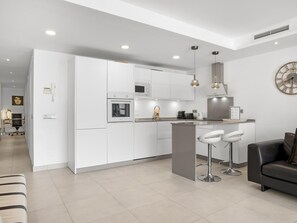 Une cuisine moderne avec des meubles blancs, un four encastré et un îlot central doté de tabourets de bar.