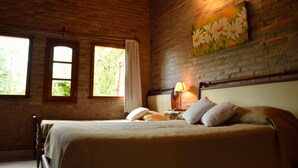 A room with a brick wall, a bed with pillows, a nightstand with a lamp, and a painting of daisies. - Hotel de campo granja el aromo (Nono)
