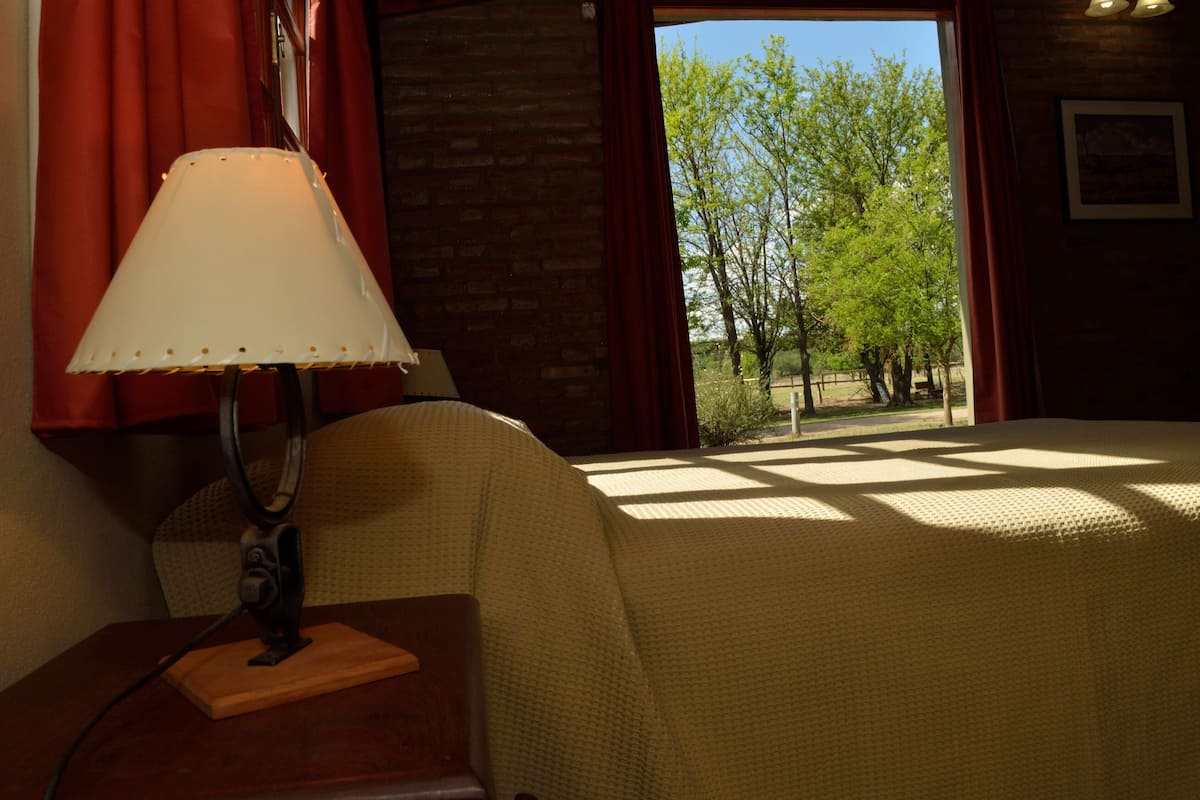 Une pièce avec un lit, une lampe et une vue sur les arbres par la fenêtre.