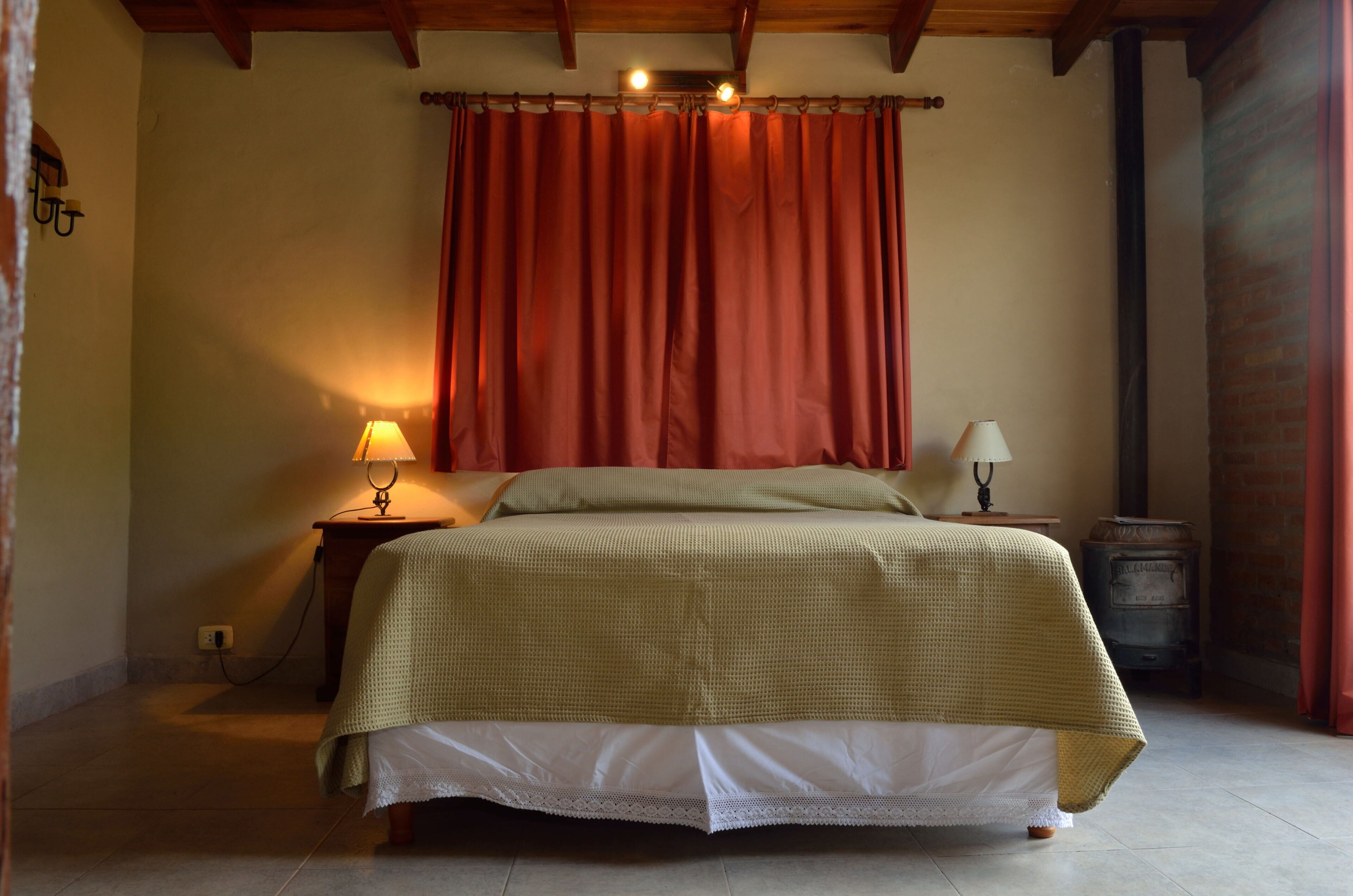 A bedroom with a bed, two bedside lamps, a heater, and a brick wall.