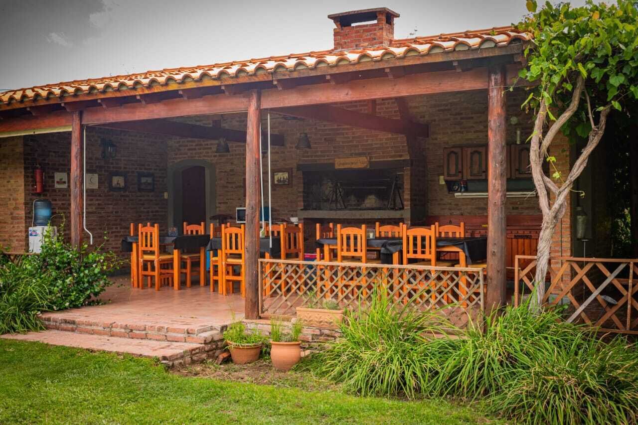 Un espacio de estar al aire libre cubierto con paredes de ladrillo y techo de tejas, rodeado de plantas en macetas y una valla de madera.