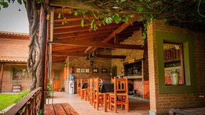 A covered outdoor seating area with wooden chairs and a long wooden table, brick walls, and a green door. - Hotel de campo granja el aromo (Nono)
