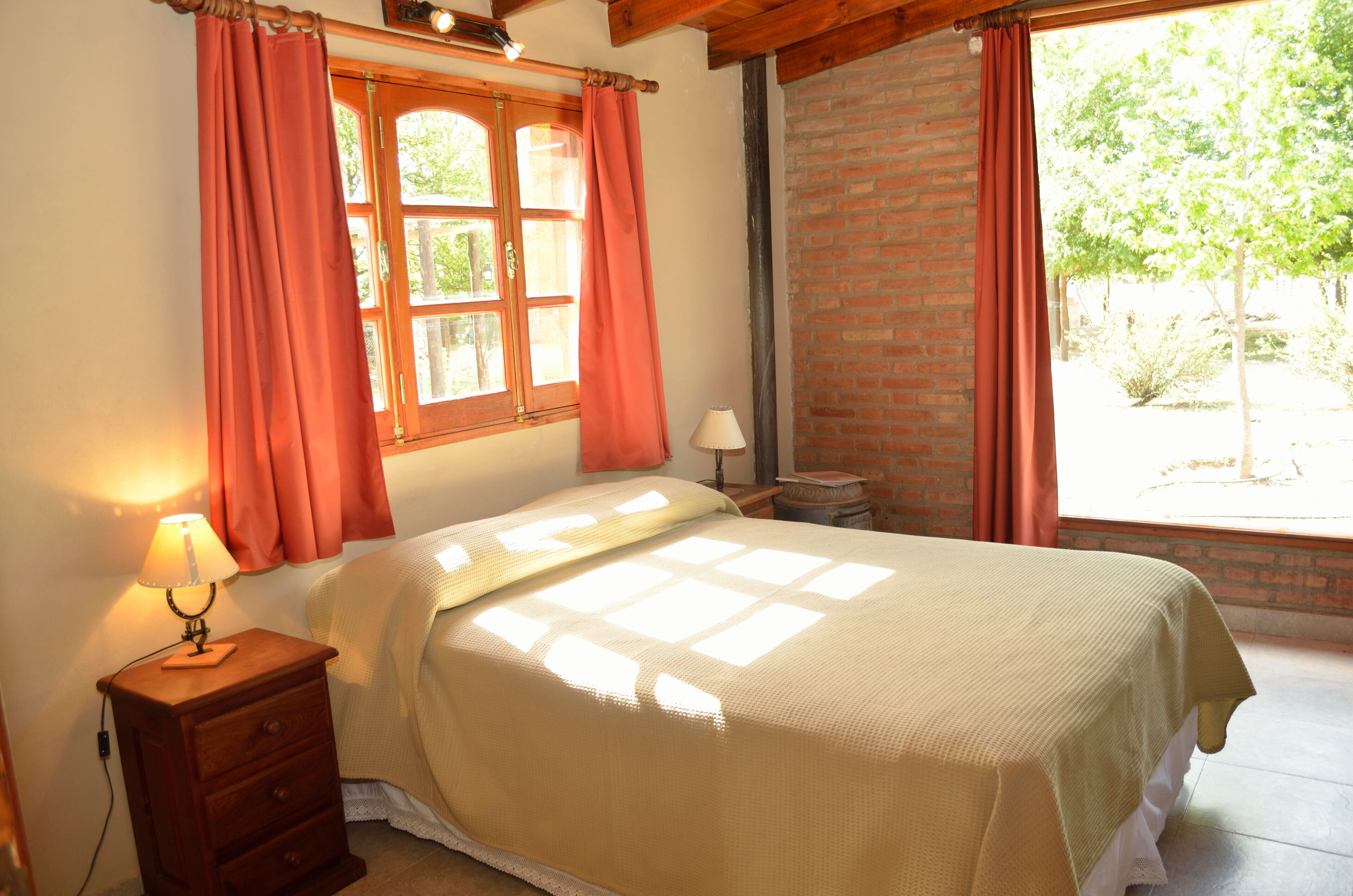 A bedroom with a bed, a nightstand, a lamp, and a window with curtains.