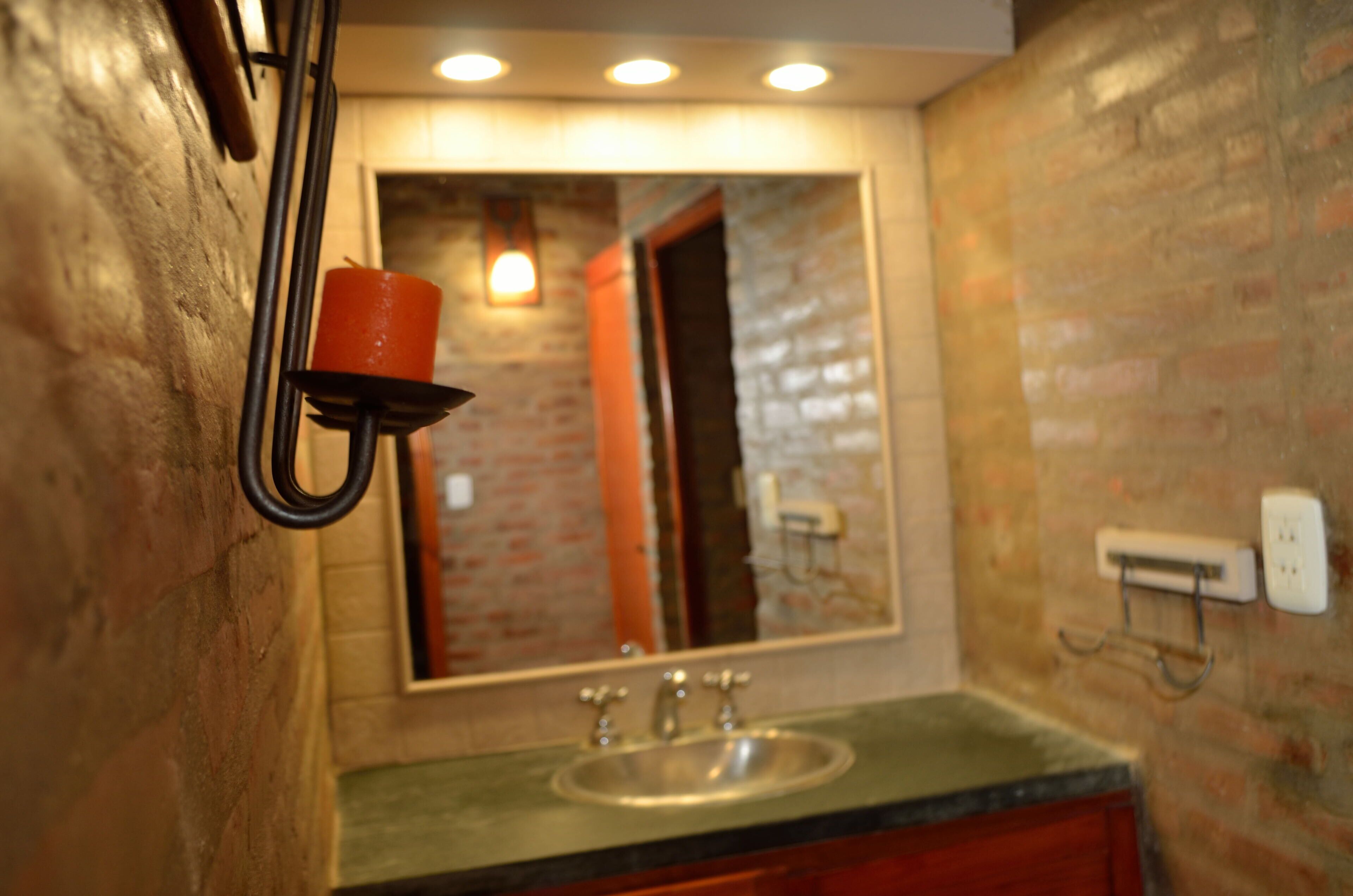 Un baño con pared de ladrillo, un lavamanos y un espejo.