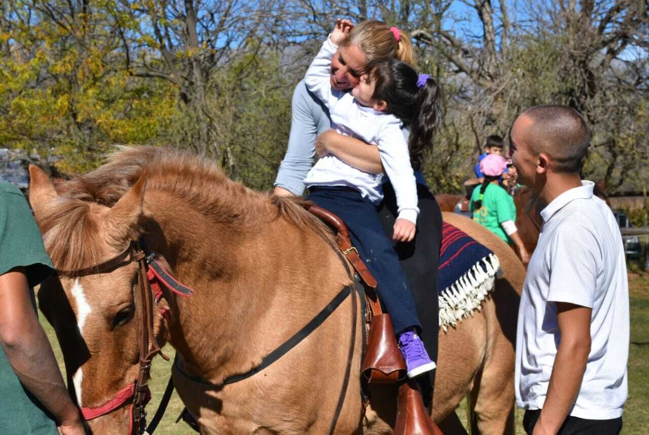 A person riding a horse with a saddle and bridle, surrounded by trees and other people.