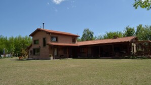A two-story house with a red-tiled roof, a covered porch, and a grassy yard. - Hotel de campo granja el aromo (Nono)