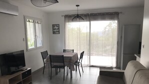 Una sala de estar con televisión, sofá, mesa de comedor, sillas y una zona de cocina con refrigerador.