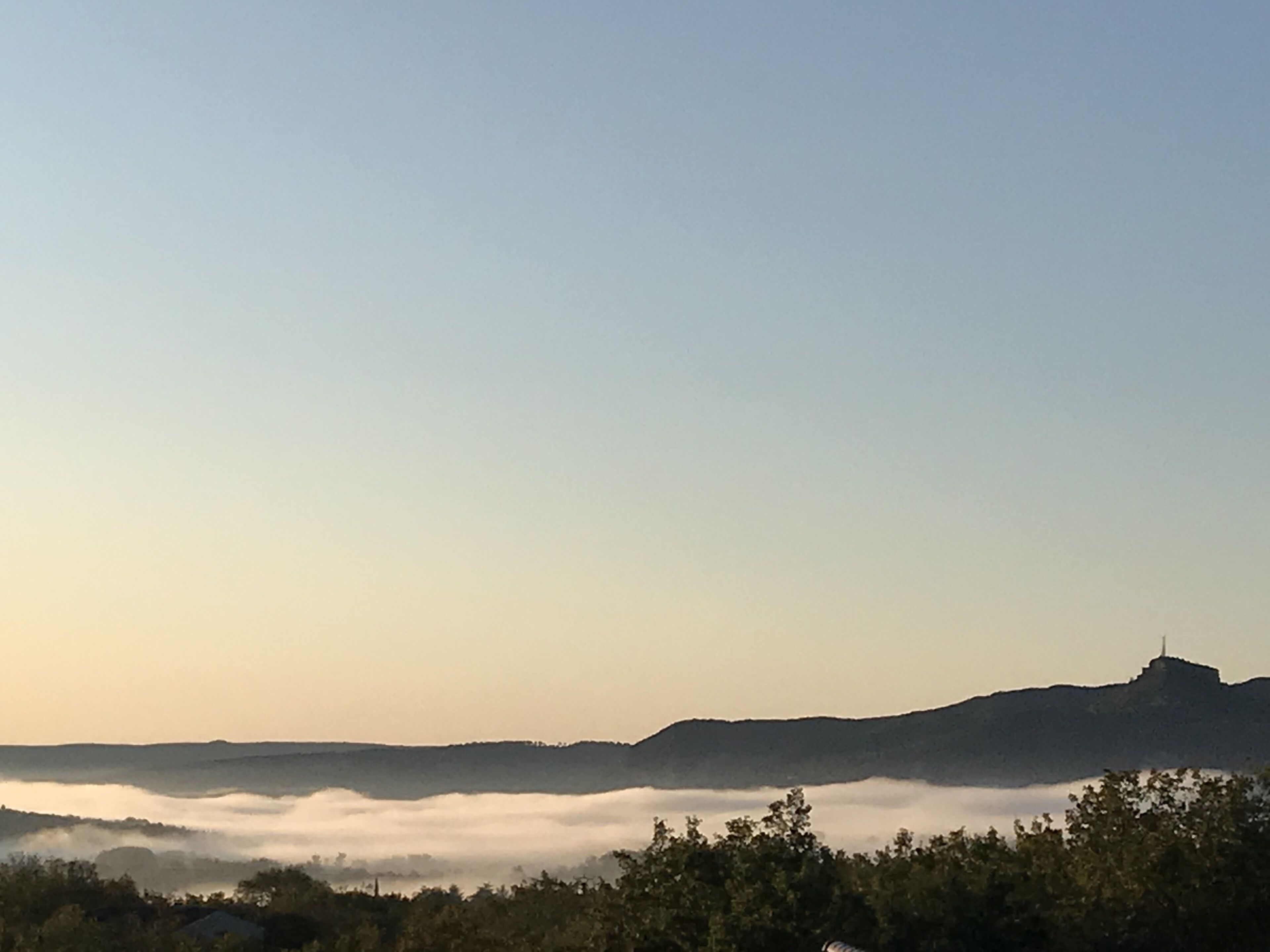 Un paisaje con una cadena montañosa, una zona boscosa y una masa de agua con niebla.
