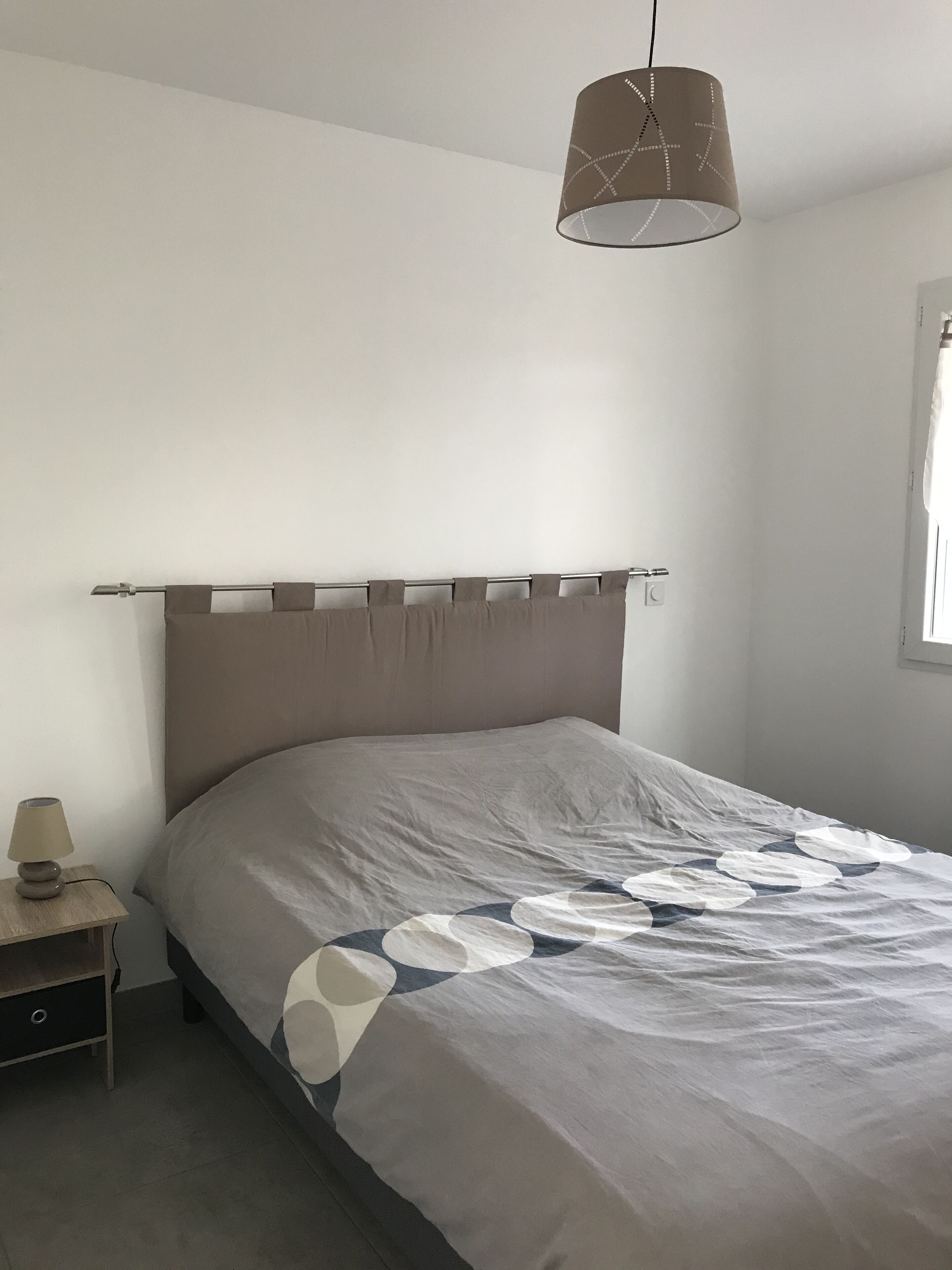 Un dormitorio con cama, mesita de noche, lámpara y una lámpara colgante.