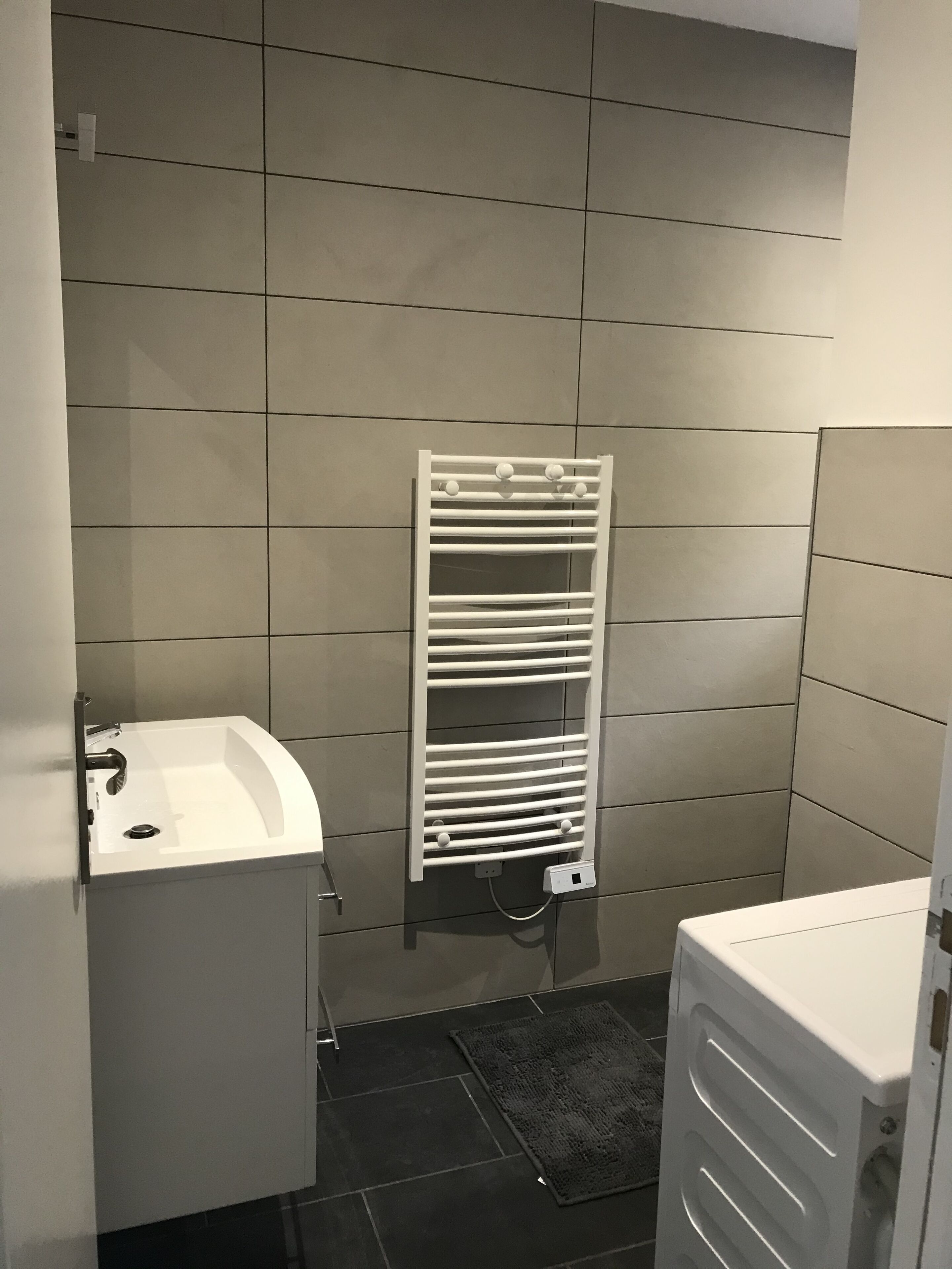 Un bagno con un lavandino bianco, un portasciugamani e un tappeto nero.