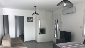 Una habitación moderna y minimalista con sofá, mesa de comedor con sillas, televisor y un ventanal grande.