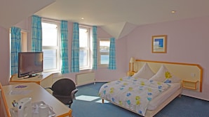 A hotel room with a bed, a desk with a computer and a chair, a TV, and a window with curtains. - Penta Hotel (Douglas)