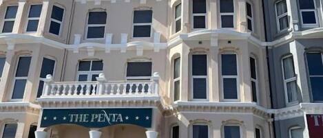 Un edificio de varios pisos con una entrada destacada, un balcón y un letrero que dice 'THE PENTA'.