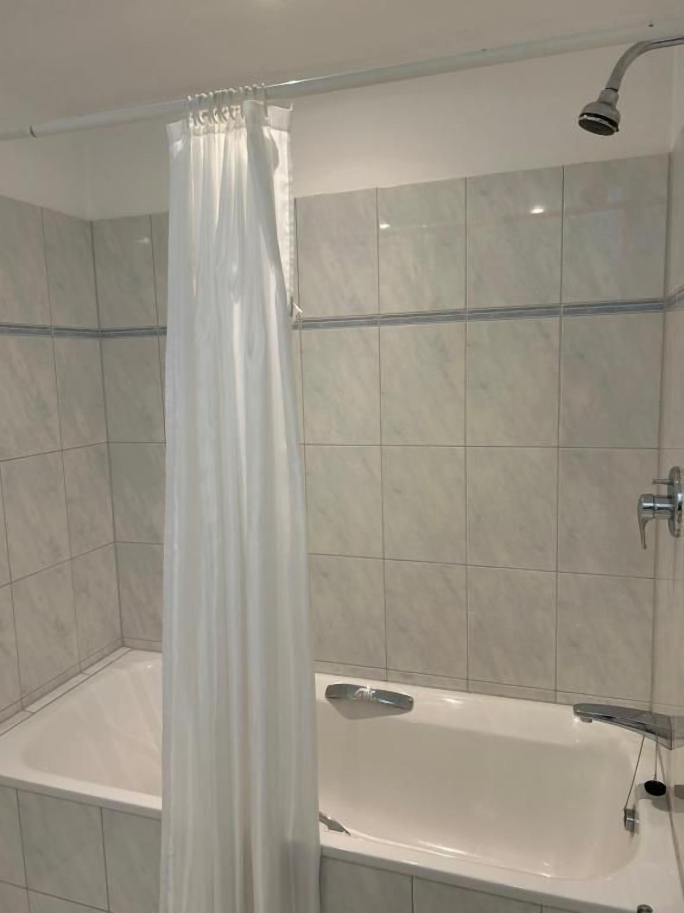 Un baño con cortina de ducha, bañera y paredes de azulejos.