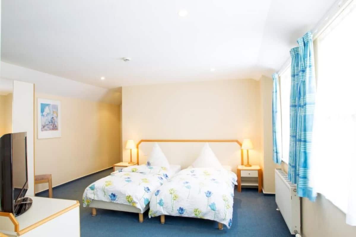 A hotel room with two beds, a TV, a desk, and a window with curtains.