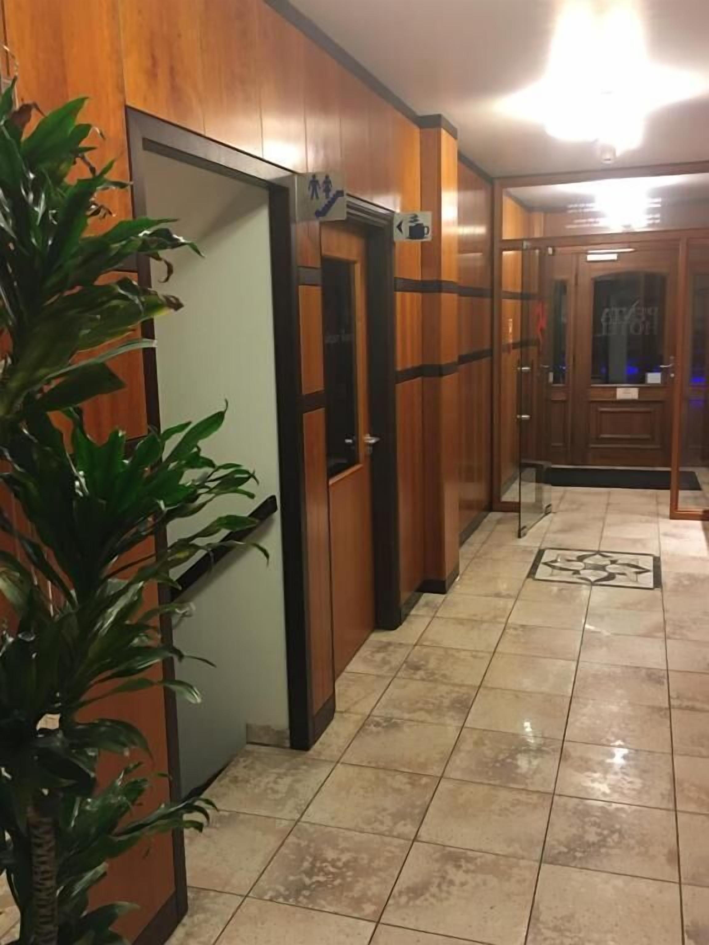 Un pasillo con paneles de madera, un ascensor de vidrio y suelo de baldosas.
