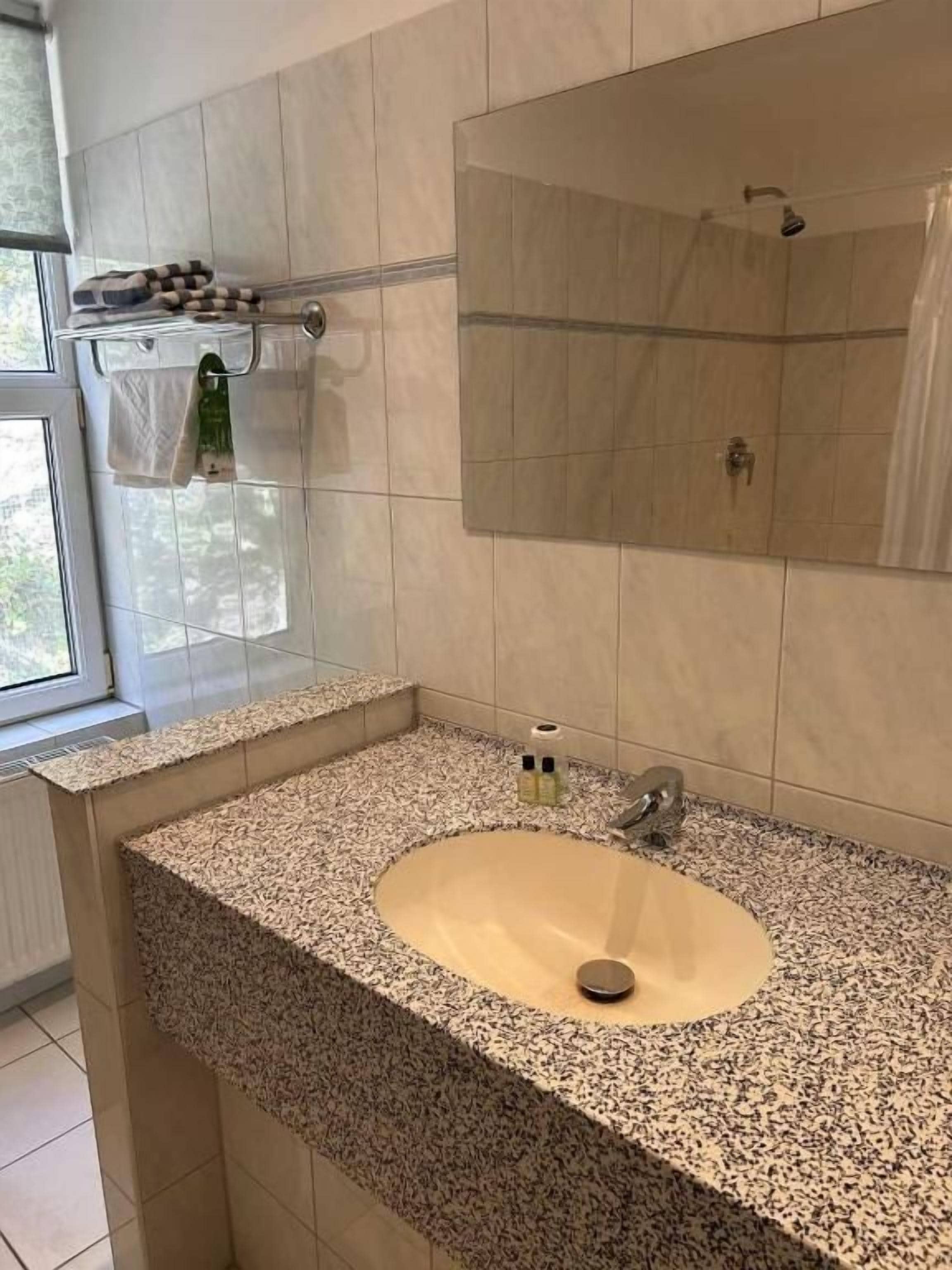 A bathroom with a granite countertop sink, a mirror, and a shower.