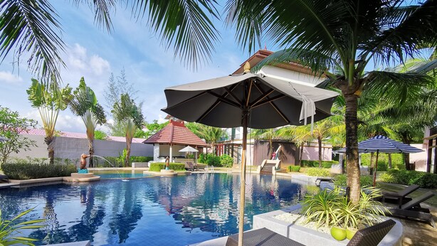 A swimming pool with lounge chairs and umbrellas, surrounded by palm trees and a small gazebo. - Apartment with private jacuzzi and pool access. Just 800 meters to the beach. (Phuket)