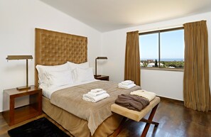 Een hotelkamer met een groot bed, twee nachtkastjes, een raam met gordijnen en uitzicht op zee.