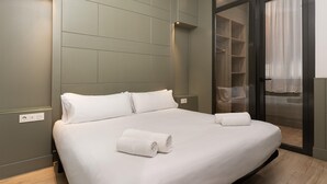 A modern hotel room with a large bed, a built-in wardrobe, and a sliding glass door to the bathroom. - Quiet and charming apartment in Gracia neighborhood (Barcelona)