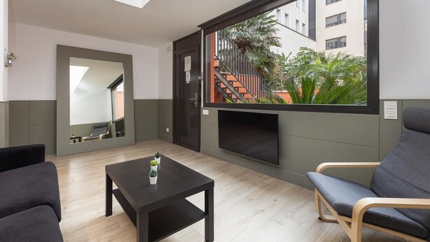 A modern living room with a large window, a flat-screen TV, a sofa, a coffee table, and a small plant. - Quiet and charming apartment in Gracia neighborhood (Barcelona)
