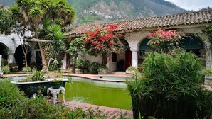 Un patio tradicional con una fuente, rodeado de exuberante vegetación y un telón de fondo montañoso.