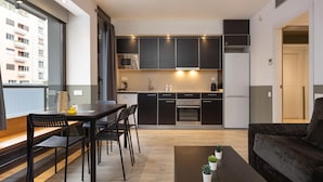 Una cocina moderna con armarios oscuros, un comedor con mesa y sillas, y una sala de estar con sofá.