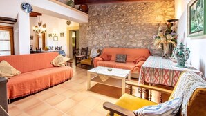 Un salon chaleureux avec un mur en pierre, un canapé, une table basse et une petite table recouverte d’une nappe à motifs.